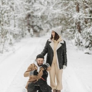 A happy couple enjoys a winter walk with their dog in a snowy forest trail.