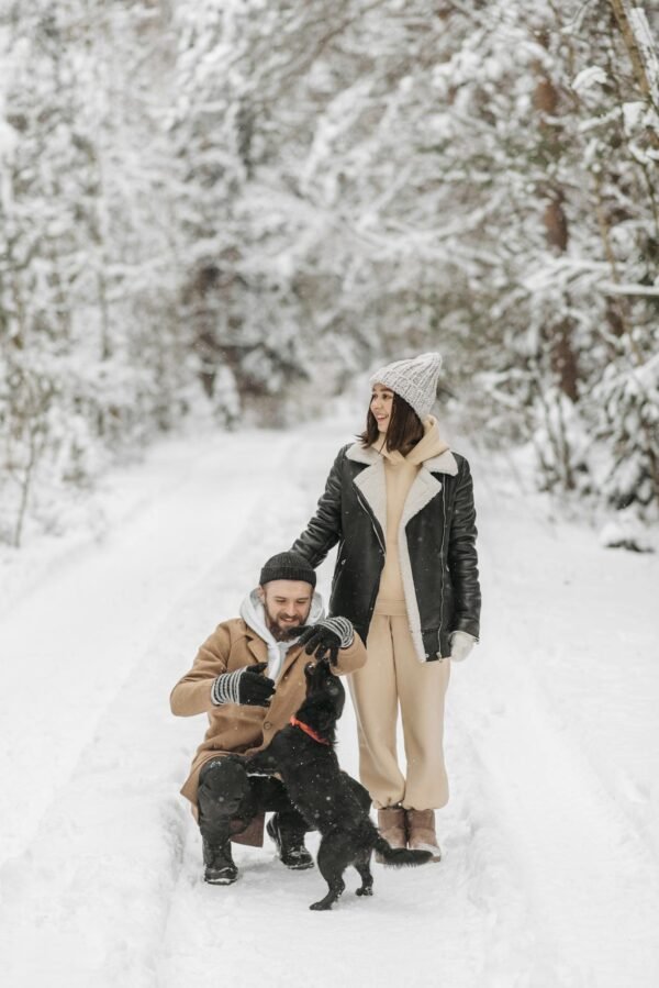 A happy couple enjoys a winter walk with their dog in a snowy forest trail.