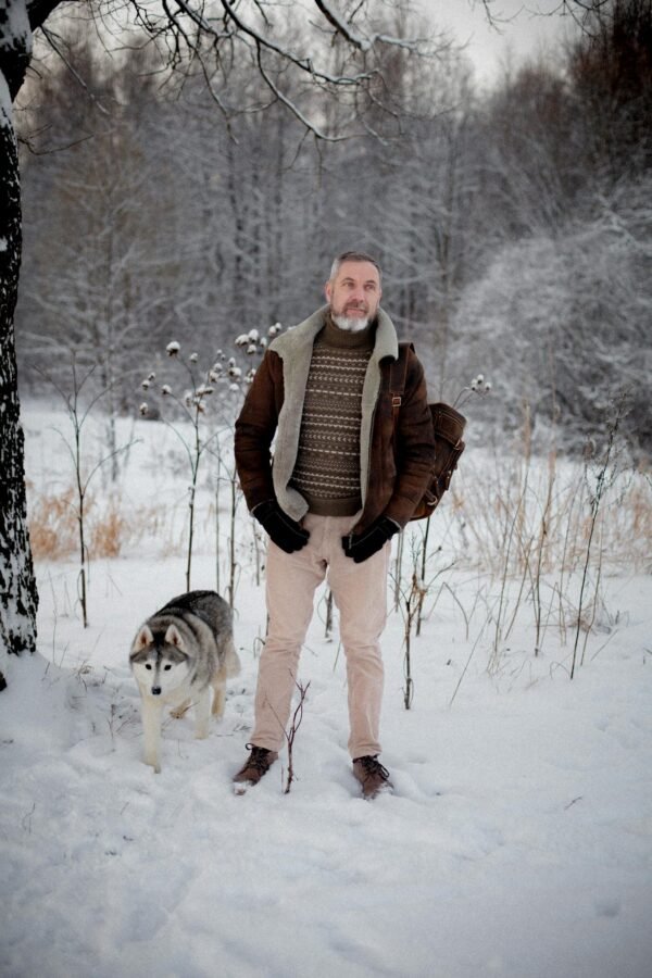 A man with a husky on a walk through a snowy winter forest scene.