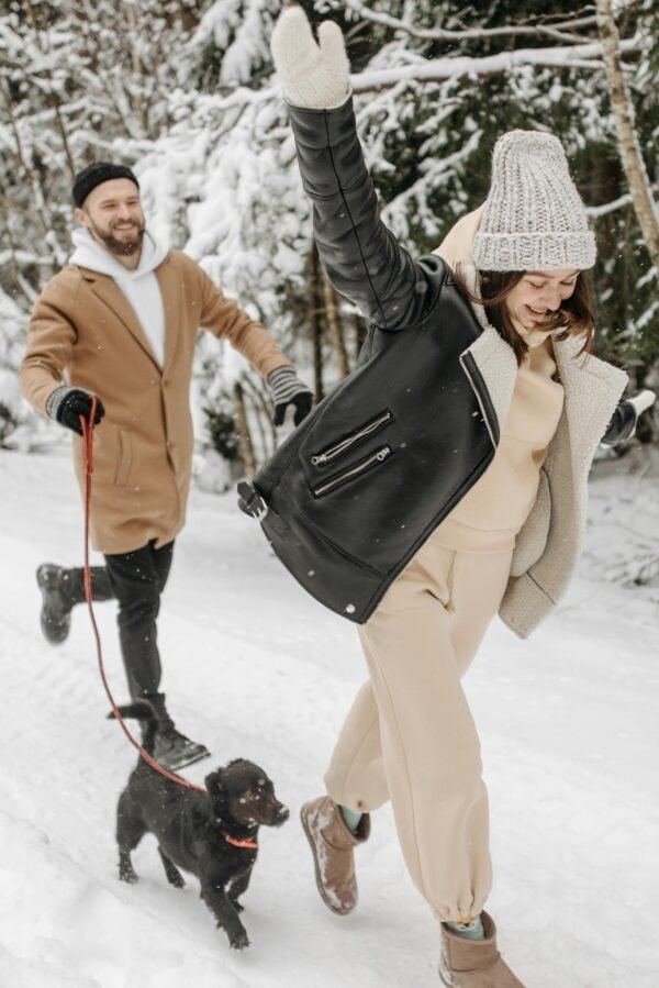 Happy couple walking their dog in a snowy winter forest, enjoying the fun and cold weather.